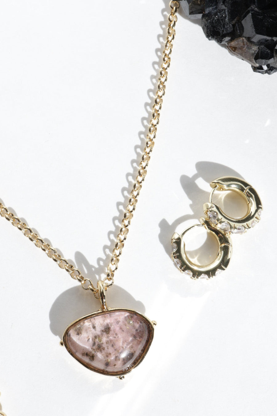 Gold necklace with a pink stone pendant on a white background
