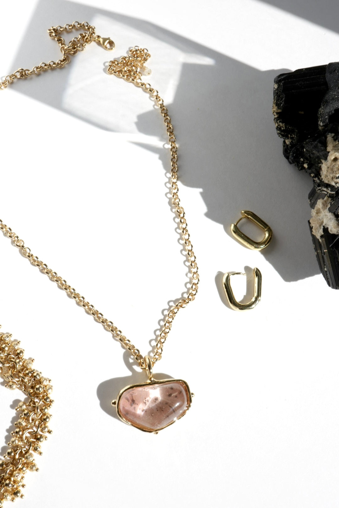 Gold necklace with a pink pendant on a white surface with crystals.