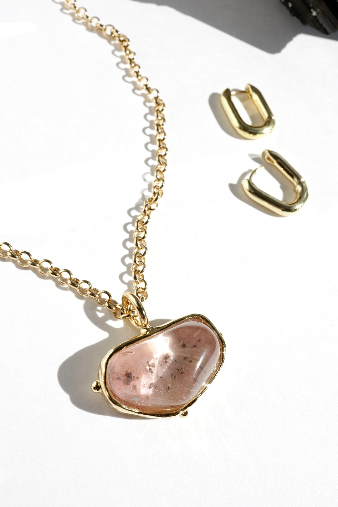 Gold necklace with a pink stone pendant and matching earrings on a white background