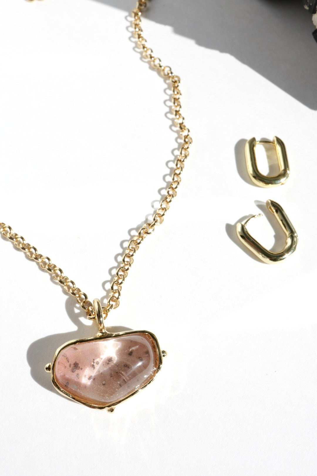 Gold necklace with a pink stone pendant and matching earrings on a white background