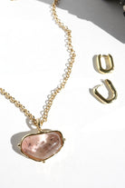Gold necklace with a pink stone pendant and matching earrings on a white background