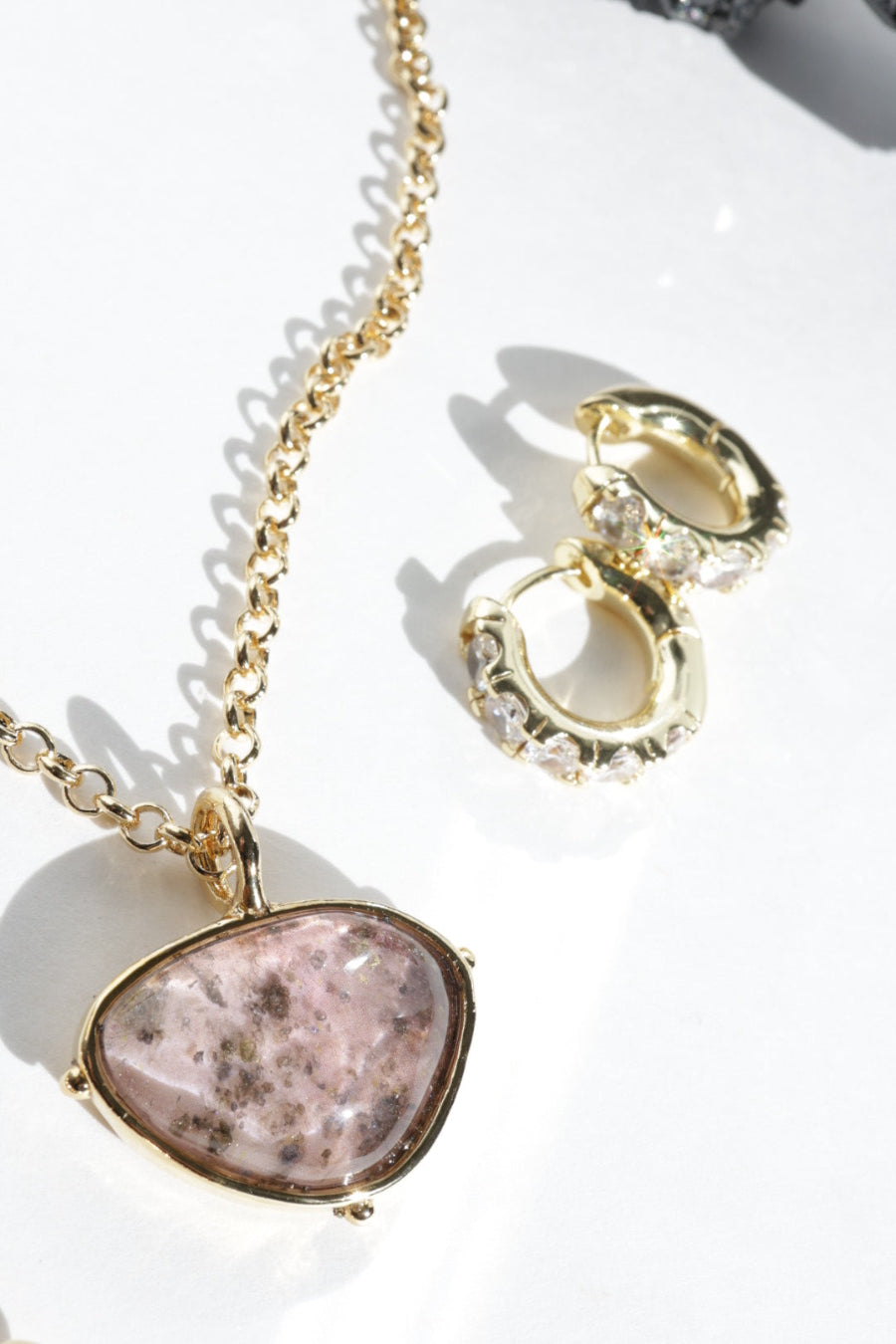 Gold necklace with a pink stone pendant and gold hoop earrings on a white background
